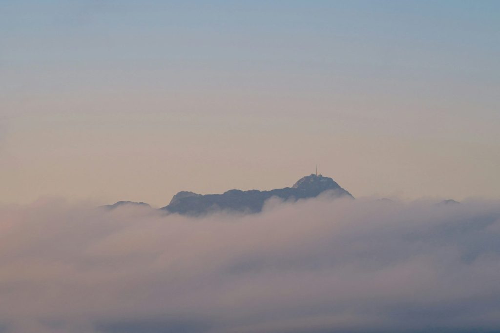 Berggipfel, der sich im Morgengrauen aus den sanften Wolken erhebt.
